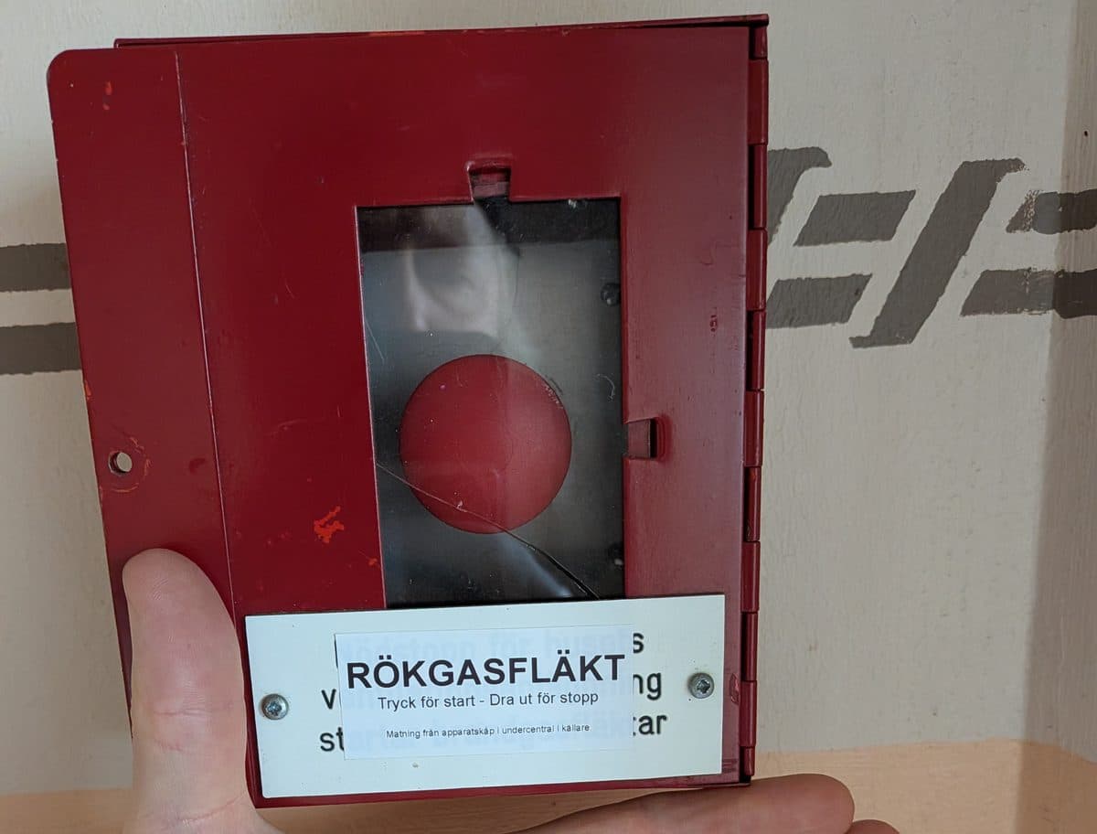 Röd startknapp för rökgasfläkt i ett trapphus